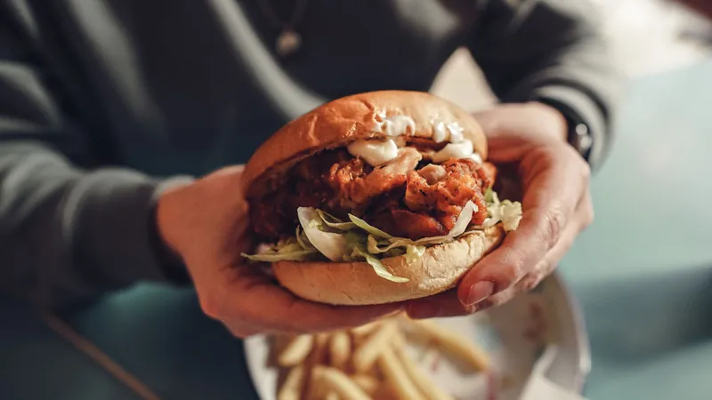 A crispy chicken burger held over a tray of chips