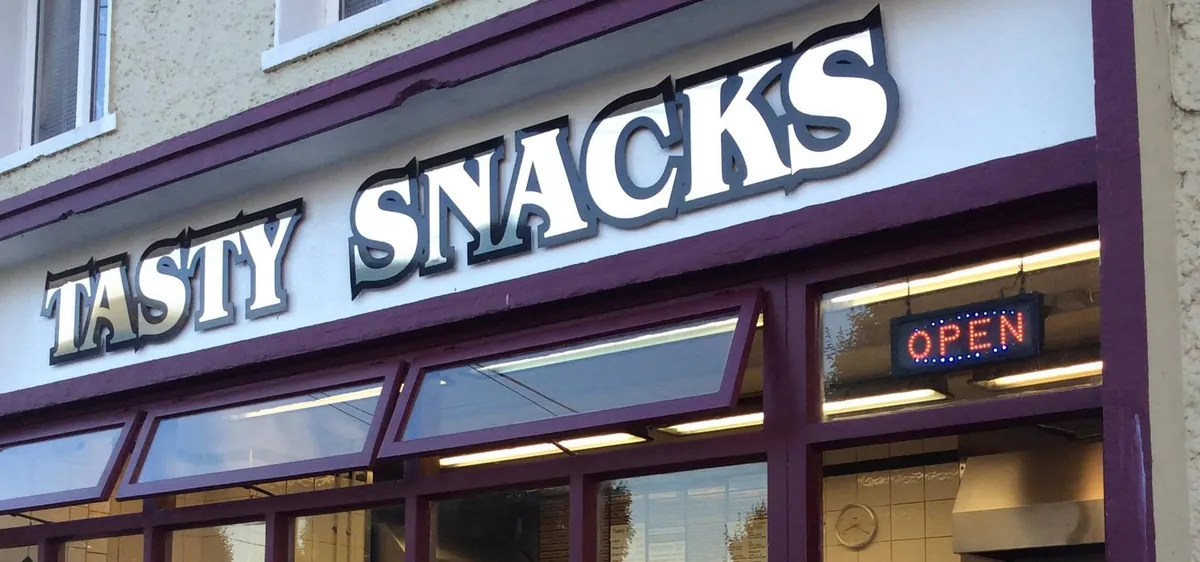 The Tasty Snacks shopfront on Knockfree Avenue in the evening, the OPEN sign lit